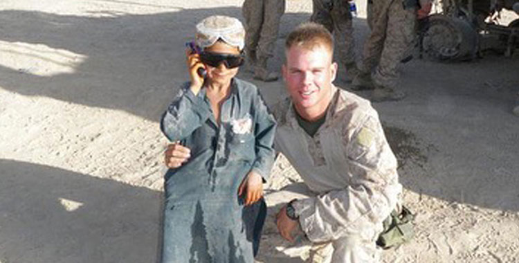 A photo of Captain Kyle Gettings in uniform posing with a kid in sunglasses.